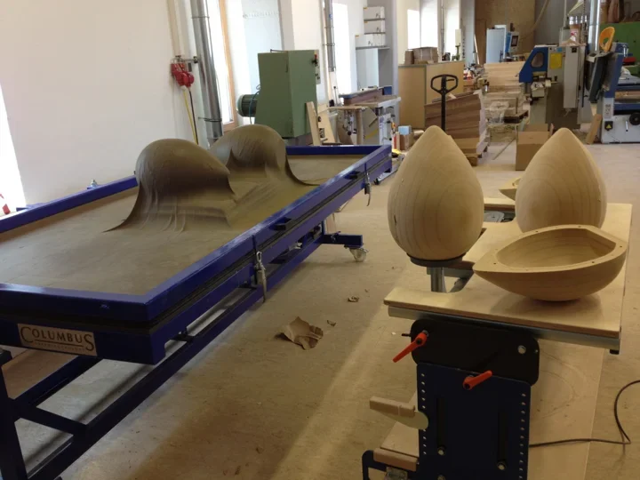 Vacuum press with a membrane over three-dimensional forms, beside shaped wooden workpieces