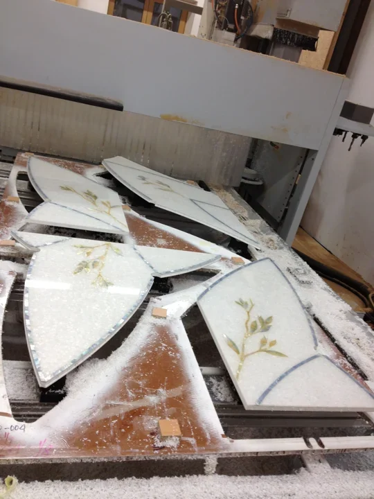 Prefabricated mother-of-pearl panels with floral motifs being trimmed to shape on a CNC machine