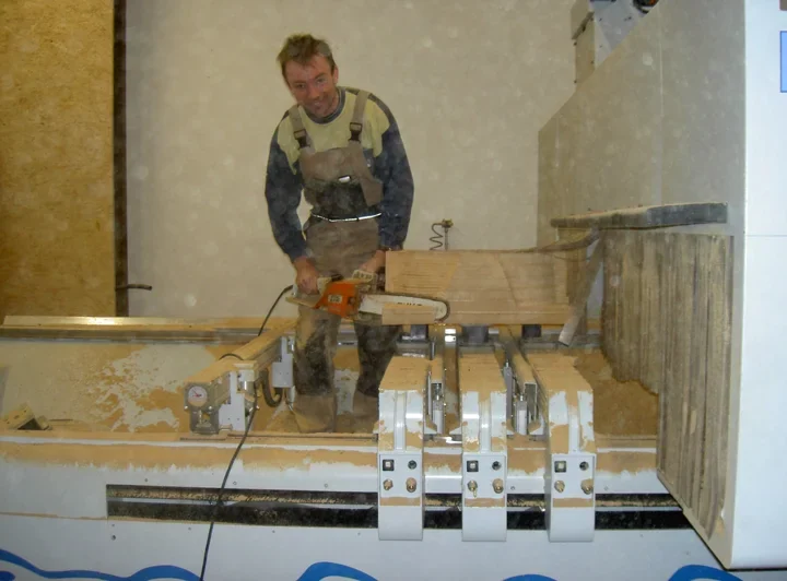 Manual rough cutting with a handheld chainsaw on a wooden workpiece clamped on the CNC machine