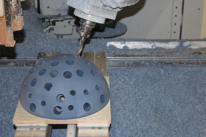Inclined milling tool machining a hemispherical component with circular openings