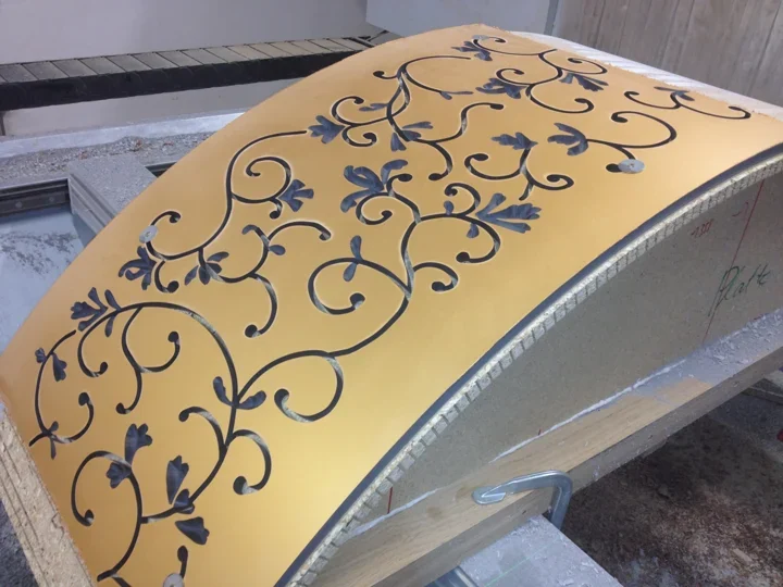 Ornamental cut-outs in a curved panel held on a machining fixture